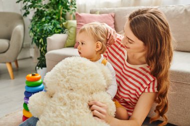 A young mother and her toddler daughter bonding over playtime with a teddy bear, creating cherished memories together. clipart