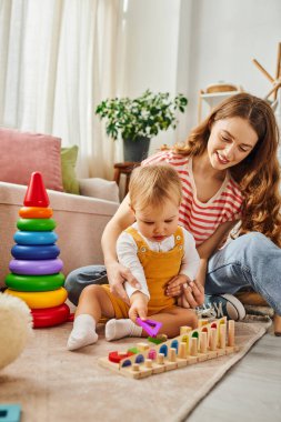 A young mother joyfully plays with her toddler daughter on the floor, bonding and creating lasting memories together. clipart