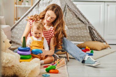 A young mother happily playing and interacting with her toddler daughter in the comfort of their home. clipart