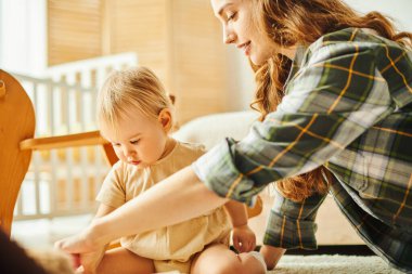 Genç bir anne, evinde yerde oynarken küçük kızıyla neşeyle etkileşime girer..