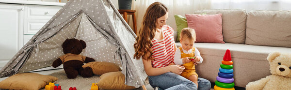 Молодая мать сидит на полу, общаясь со своей дочкой-малышкой в душевный момент общения и любви..