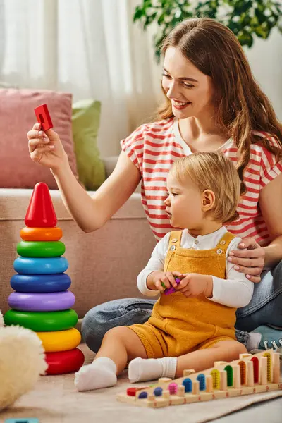 stock image A young mother and her toddler daughter share a heartwarming moment, playing together on the floor in their home.