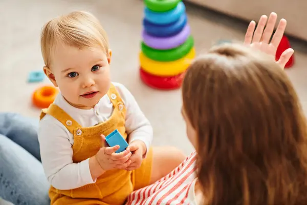 stock image A baby girl and her mother interact, playing joyfully on the floor at home.