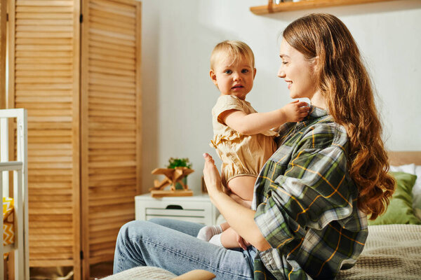 Молодая мать сидит на кровати, колышет свою маленькую дочь на руках, разделяя прекрасный и нежный момент вместе.