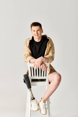 Protez bacaklı yakışıklı bir adam güvenli bir şekilde beyaz bir sandalyede oturuyor..