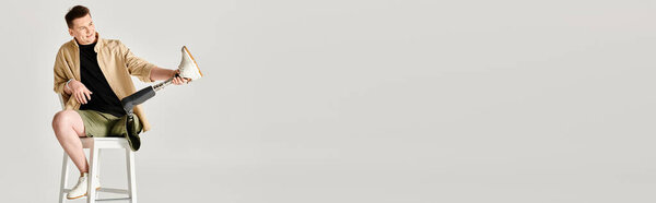 A handsome man with a prosthetic leg sits actively on top of a metal stool.