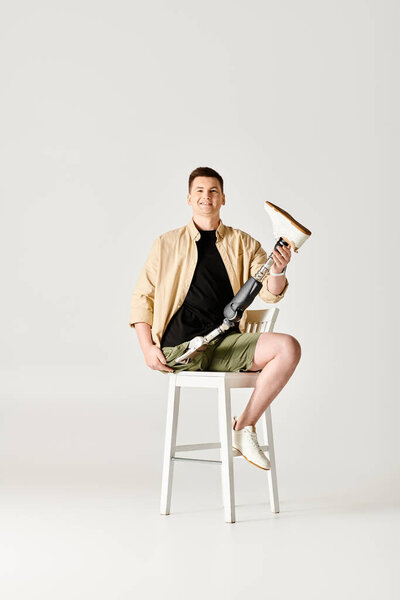 A handsome man with a prosthetic leg confidently sits on top of a white chair.