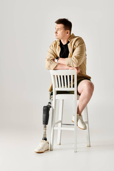 Красивый мужчина с протезной ногой активно позирует на белом стуле..