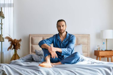 Yakışıklı bir adam yoga yapıyor, ayaklarıyla yatakta oturuyor..