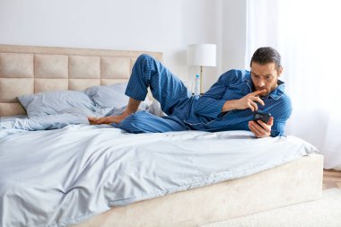 Yakışıklı adam yatağa uzanıyor, cep telefonu tutarken yoga yapıyor..