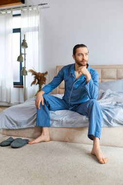A handsome man in pajamas sits calmly on a bed. clipart
