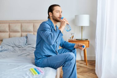 A man sitting on a bed, hydrating with water from a bottle. clipart
