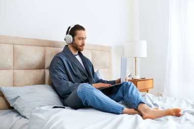 Handsome man sit on bed, wearing headphones, enjoying music. clipart