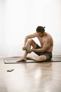 Yoga minderinde oturan yakışıklı adam, masaj topunu sakin bir şekilde tutuyor..
