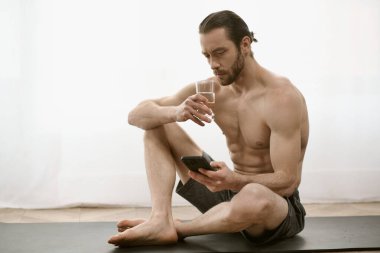 Üstsüz adam yoga minderinde oturuyor, cep telefonuna bakıyor..