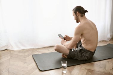 Yoga minderinde oturan bir adam, cep telefonu kullanıyor..