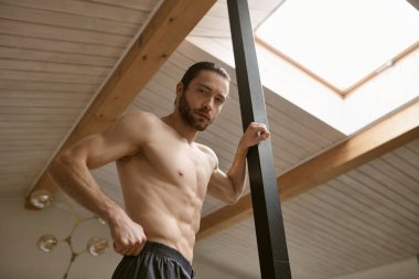 Shirtless man confidently posing at home, showcasing his strength. clipart