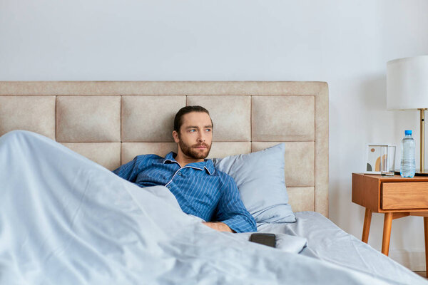 A man lying in bed covered with a blanket.