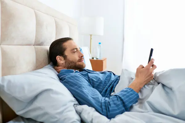 男は平和的にベッドに横たわっている間に携帯電話をチェック — ストック写真