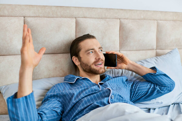A man peacefully lays in bed, focused on his cell phone call.