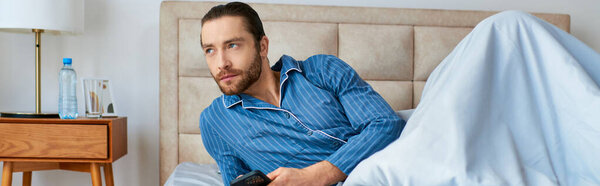 A man peacefully lays in bed, holding a remote control in his hand, enjoying a serene moment.