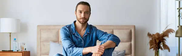 stock image A handsome man in a bedroom, peacefully sitting on top of a bed.