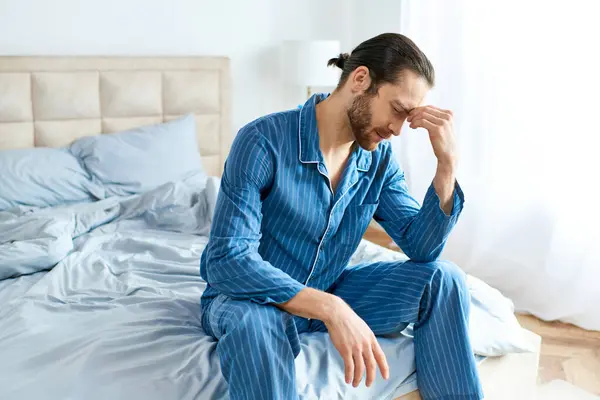 stock image A handsome man in pajamas peacefully sits on a bed.