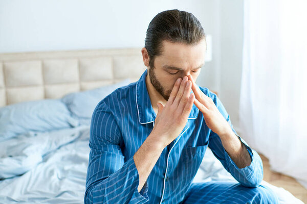 Handsome man sitting on bed, covering face with hands in a moment of introspection.