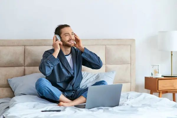 stock image Man sitting on bed, engaging in music in headphones.