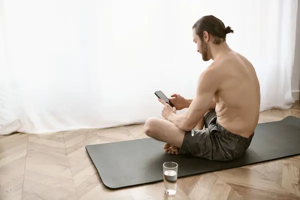 一个男人坐在瑜伽垫上 用手机 — 图库照片