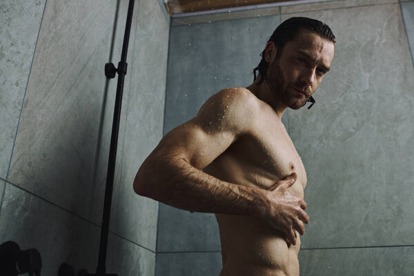 Мужчина без рубашки принимает душ перед зеркалом.