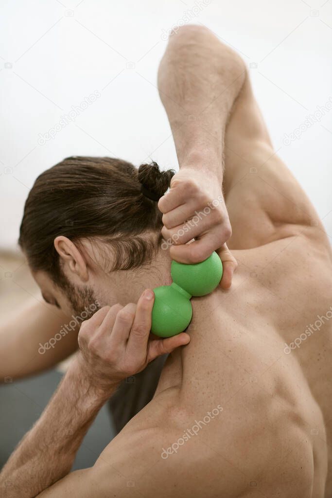 A handsome man doing yoga at home, holding a green massage ball in his right hand.