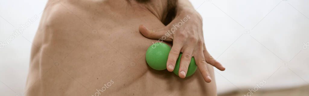 A man peacefully holds a green massage ball in his right hand while practicing yoga at home.