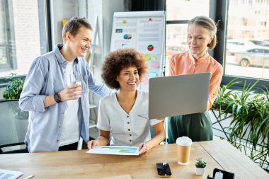 Modern bir ofis ortamında dizüstü bilgisayarın etrafında beyin fırtınası yapan çalışkan iş kadınlarından oluşan çeşitli bir grup..