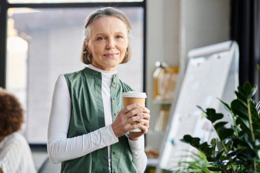 Businesswoman holds a coffee cup and looking at camera. clipart