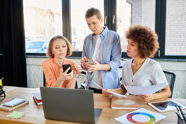 Инновационные женщины, сидящие вместе, погруженные в обсуждение мобильных телефонов.