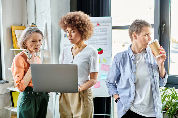 Группа разноплановых, трудолюбивых деловых женщин собирается вокруг ноутбука в коворкинг-пространстве.