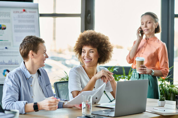 Разнообразные женщины-профессионалы, работающие вместе над ноутбуком за современным столом.