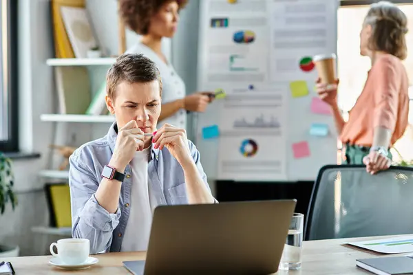 stock image A businesswoman engrossed in work on a laptop computer, with her diverse colleagues on backdrop.