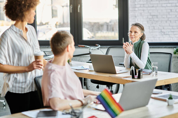 Motivated diverse businesswomen working together on project in office, pride flag.