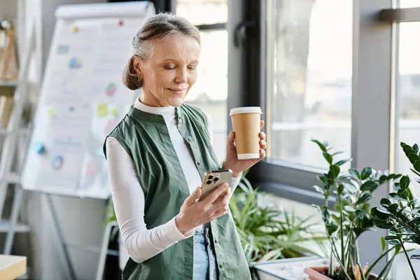 stock image A woman multitasks coffee and phone in a busy office.