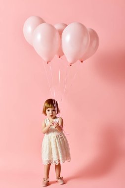 Adorable girl in white dress holding pink balloons on a pink background. clipart