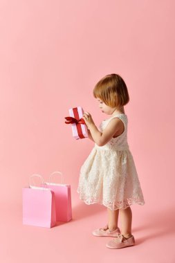Beyaz elbiseli küçük kız neşeyle pembe bir hediye kutusu tutuyor..