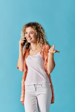 Çekici genç bir kadın mavi arka planda cep telefonuyla konuşuyor..
