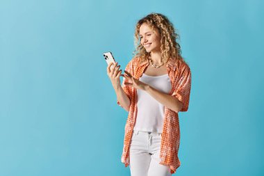 Mavi arka planda cep telefonu kullanan kıvırcık saçlı genç bir kadın..