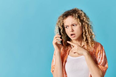 Kıvırcık saçlı genç bir kadın cep telefonuyla konuşuyor..