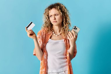 Elinde kredi kartı ve cep telefonu olan kıvırcık saçlı bir kadın..