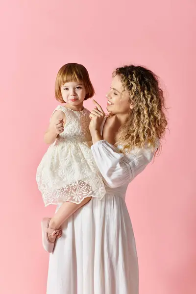 Woman White Dress Cradles Little Girl Pink Background — ストック写真
