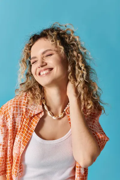 stock image A young woman with curly hair smiles brightly against a vibrant blue backdrop.