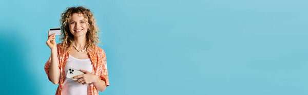 Стильная женщина держит кредитную карту на ярком синем фоне.